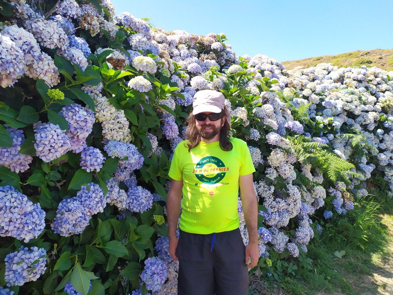 Photo de Nico devant d'énormes fleurs colorées aussi hautes que lui à Belle île en mer.