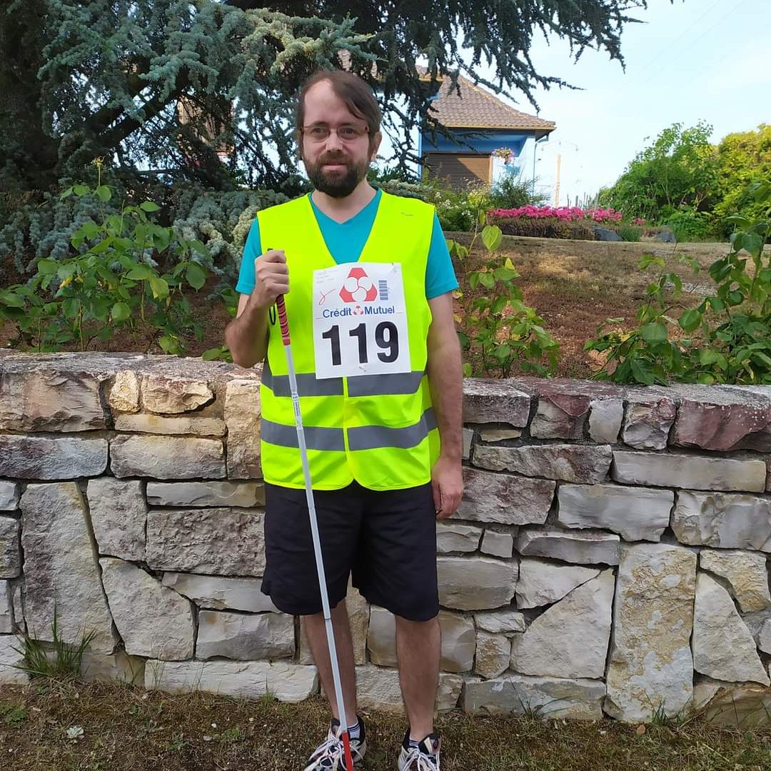 Nicolas Linder handi routard se prépare avant la course, il porte un gilet jaune de sécurité avec la mention malvoyant