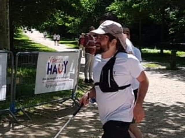 Photo De Nico en train de courir sur un chemin forestier avec sa canne en avant et une casquette saharienne