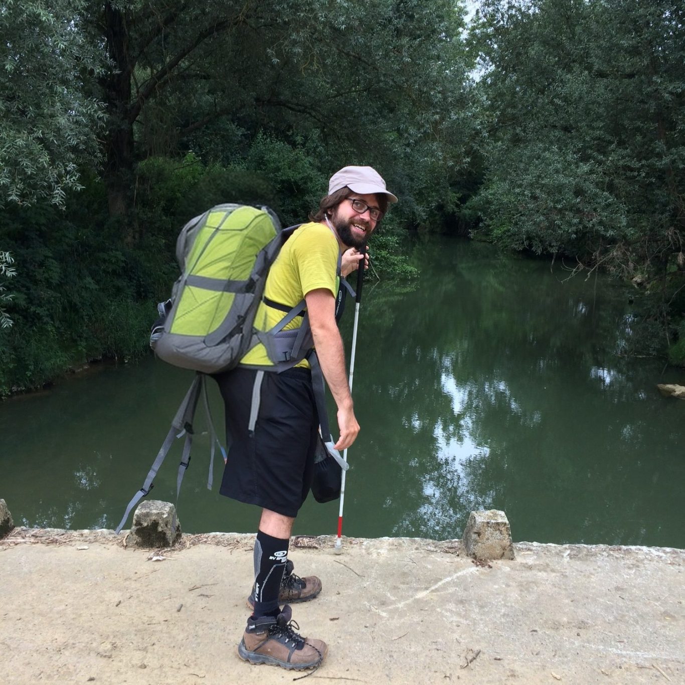 Photo de Nicolas Linder, randonnant, de profil, un sac à dos beaucoup trop gros sur le dos. Il a des protections aux mollets.